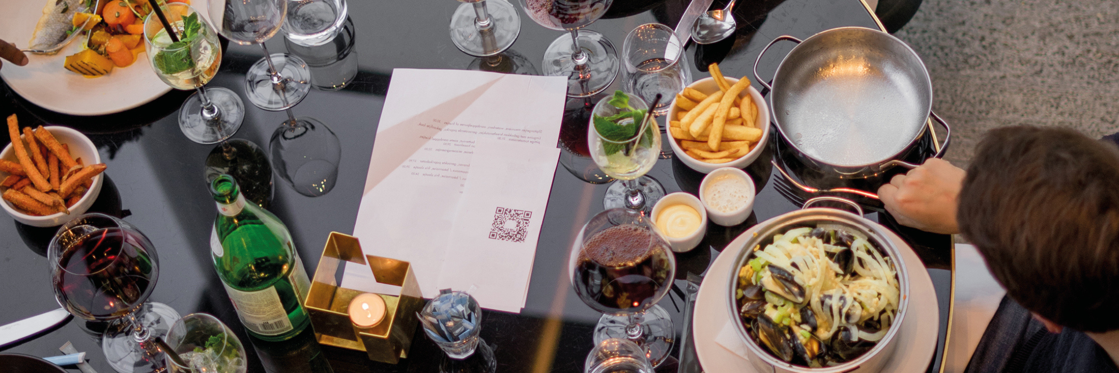 Afbeelding van een tafel vol glazen met drank in en borden met eten op.
